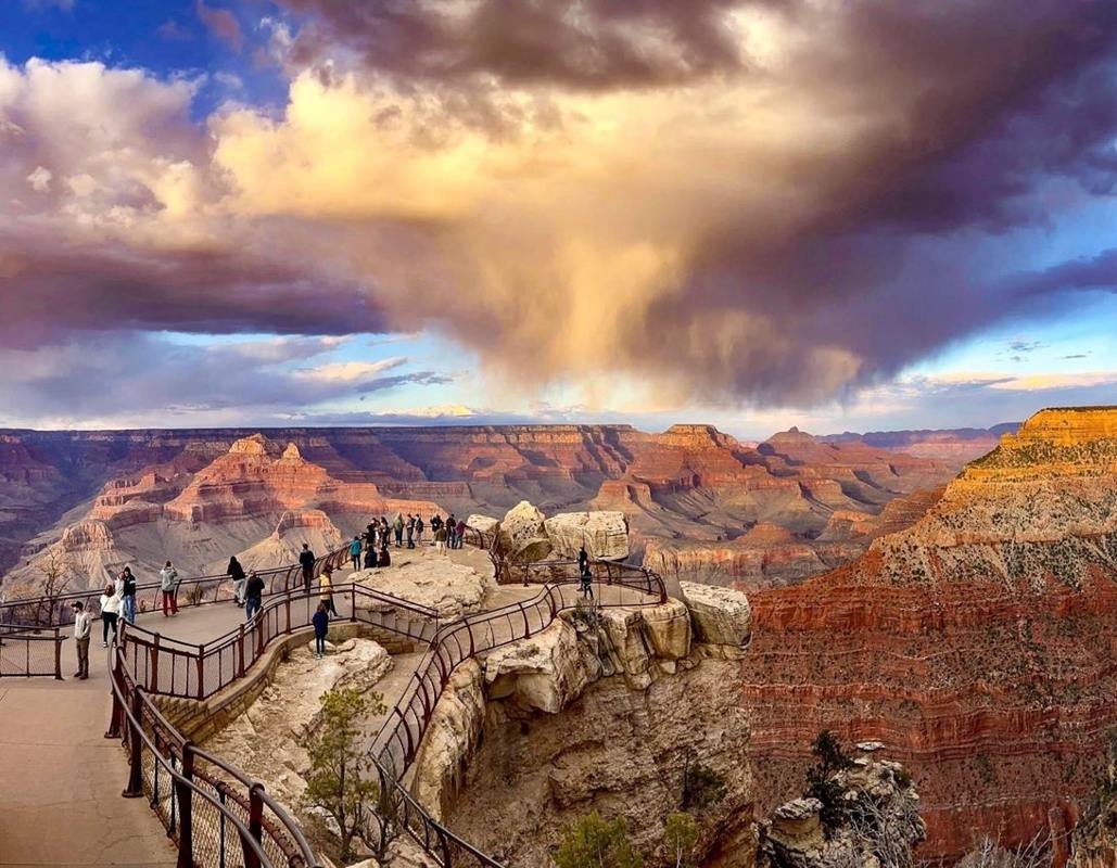 At Sunset, swirling rain clouds above a vast canyon filled with colorful peaks and cliff walls.