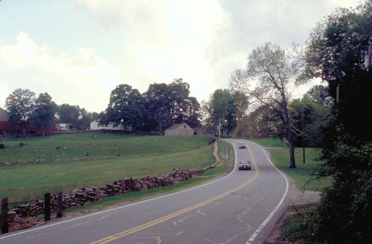 Soft lights at dusk heighten the serenity of the Byway. A cobblestone fence borders a farm field and lines the road.